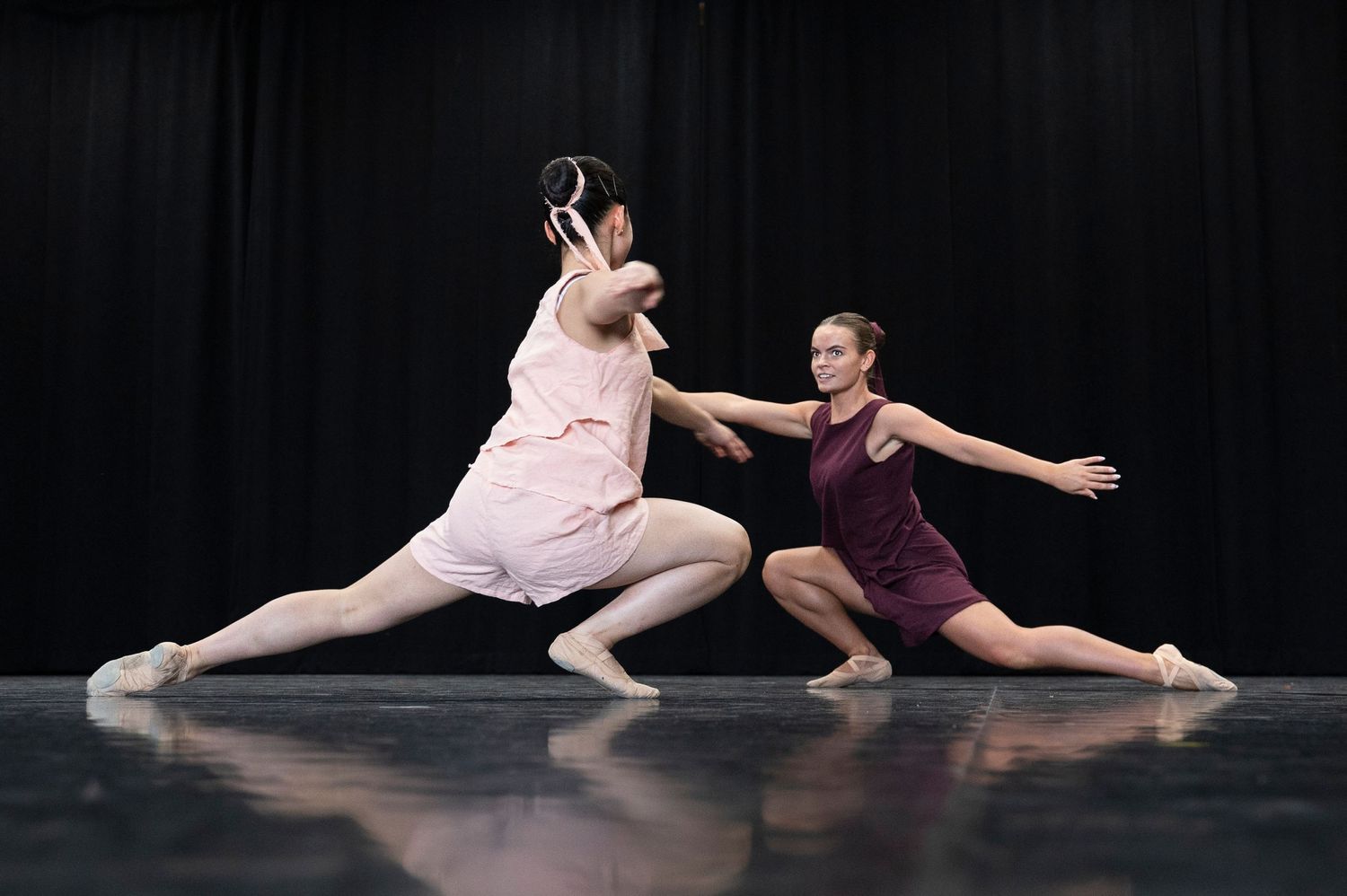 Two contemporary dancers performing dramatic movements on dark stage.