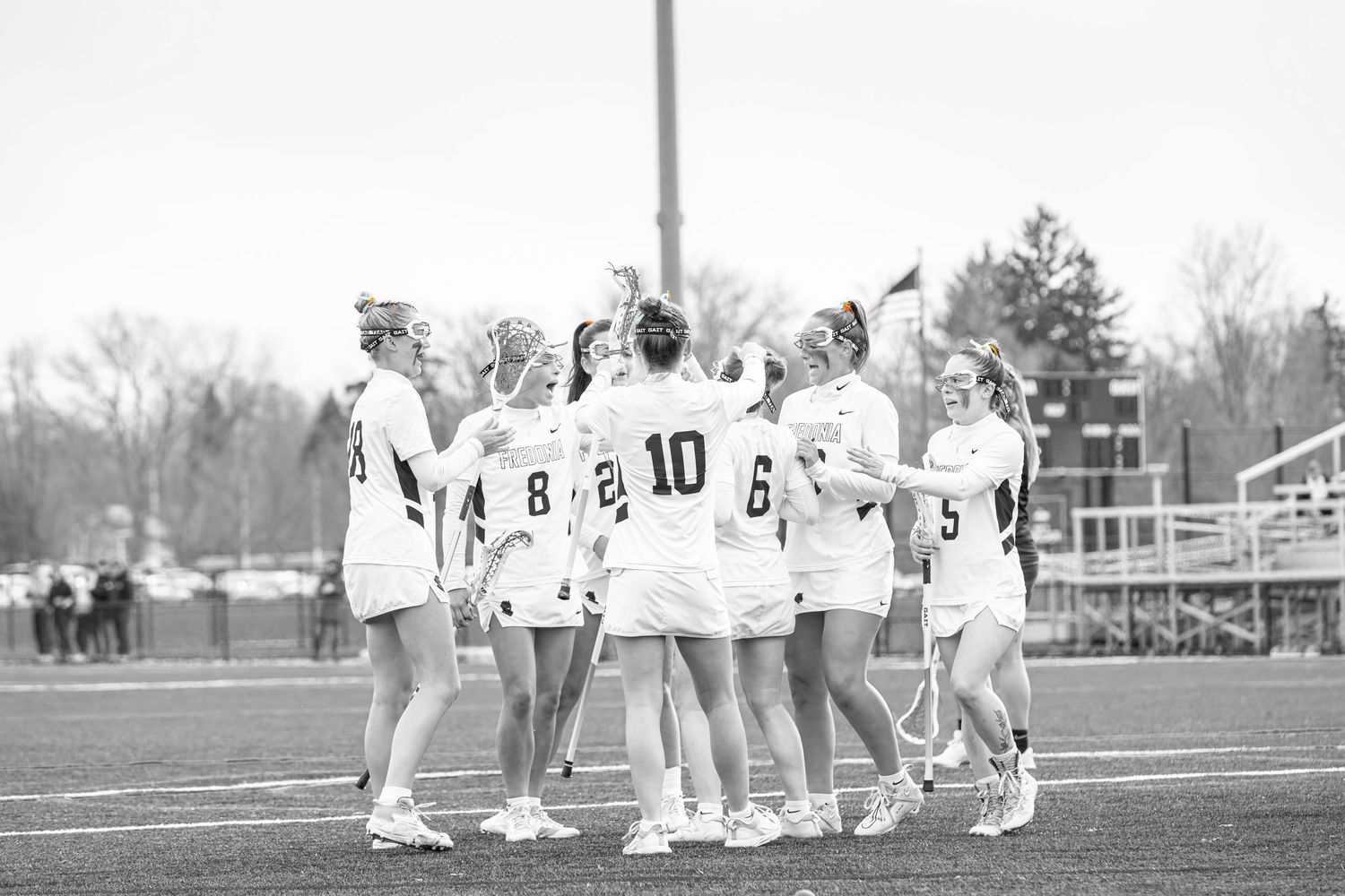 Players line up in formation during a lacrosse game on a sunny day at the sports field.