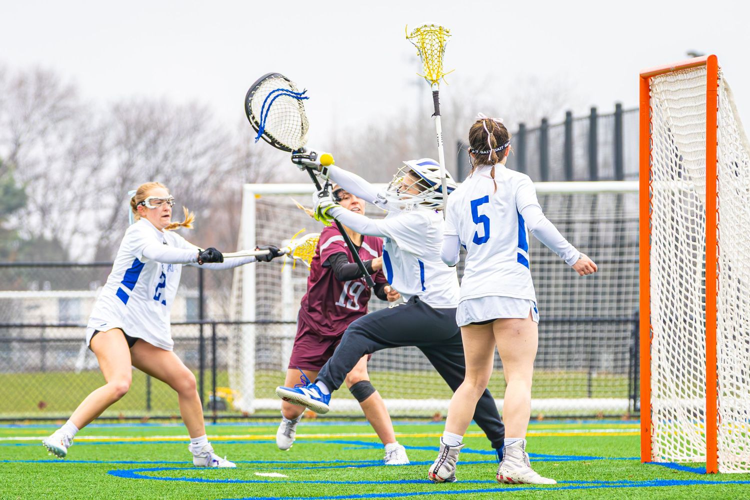 Lacrosse players compete near the goal during an intense match on a sports field.