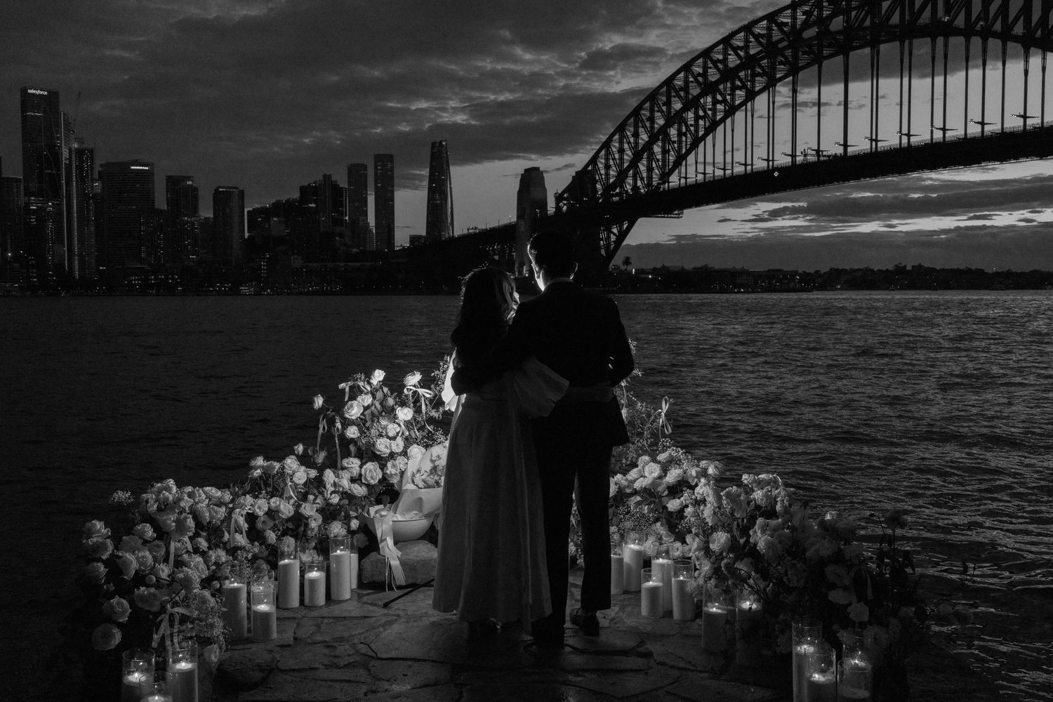 Iconic Sydney Harbour Bridge silhouetted against dramatic cloudy skies during sunset over the harbor waters.