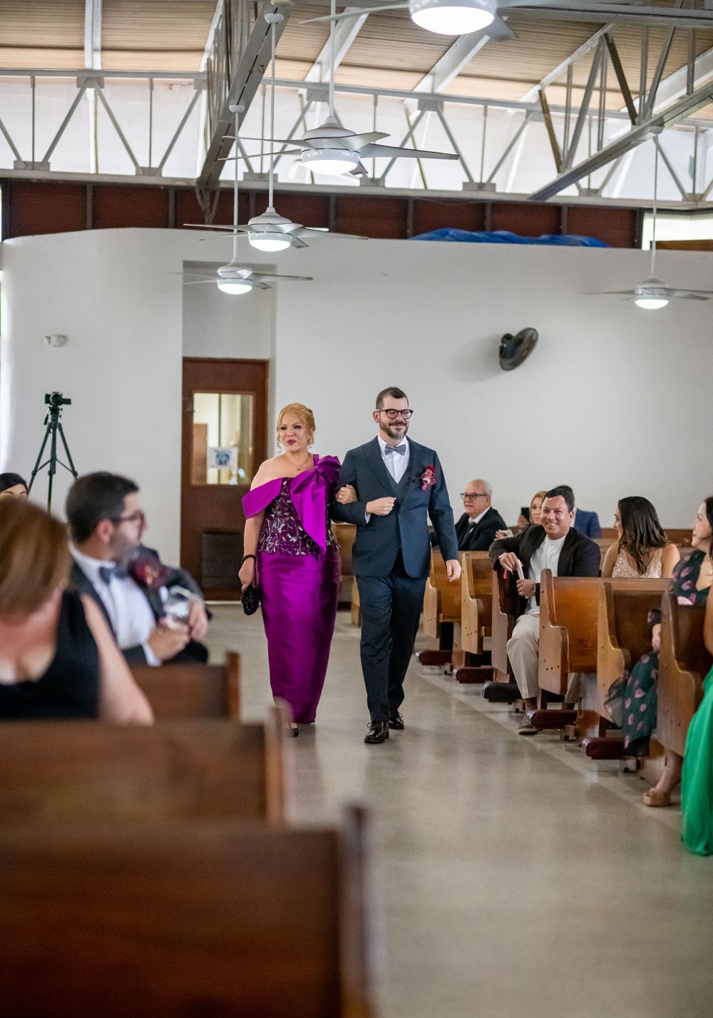 Wedding guests watch as couple walks down church aisle during ceremony.