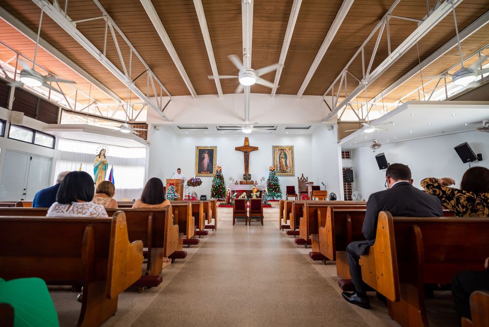 Interior of Catholic church with wooden pews and exposed beam ceiling during ceremony.