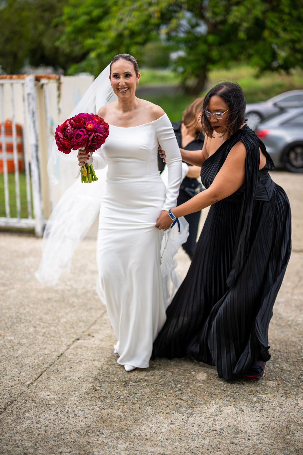 Wedding party members adjust bride's dress outside venue.