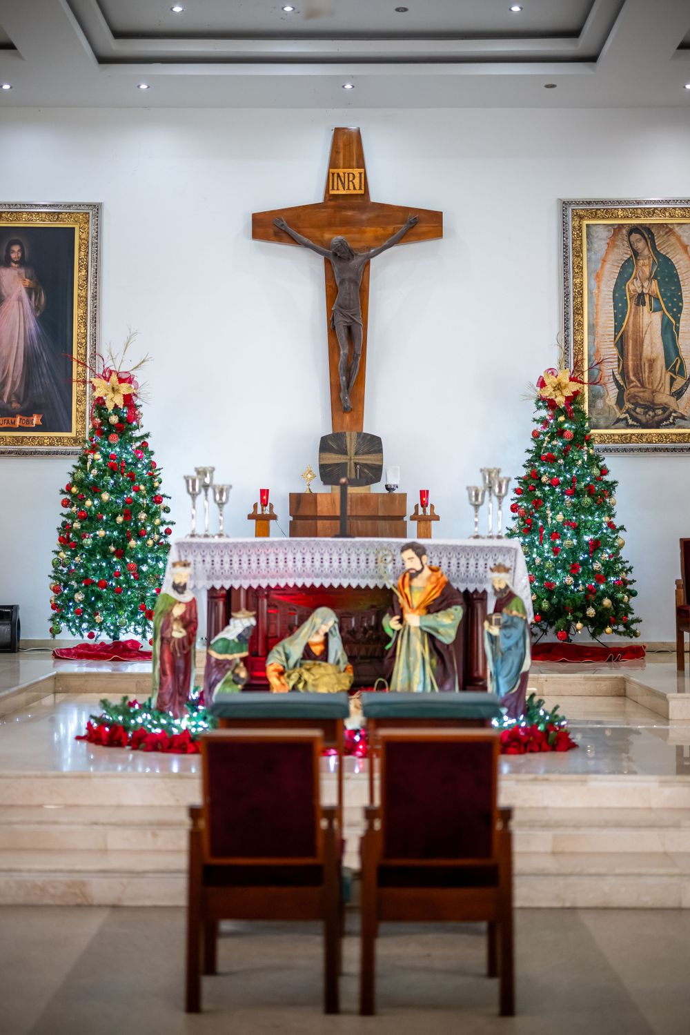 Christmas-decorated church altar with crucifix, nativity scene, and two decorated trees.