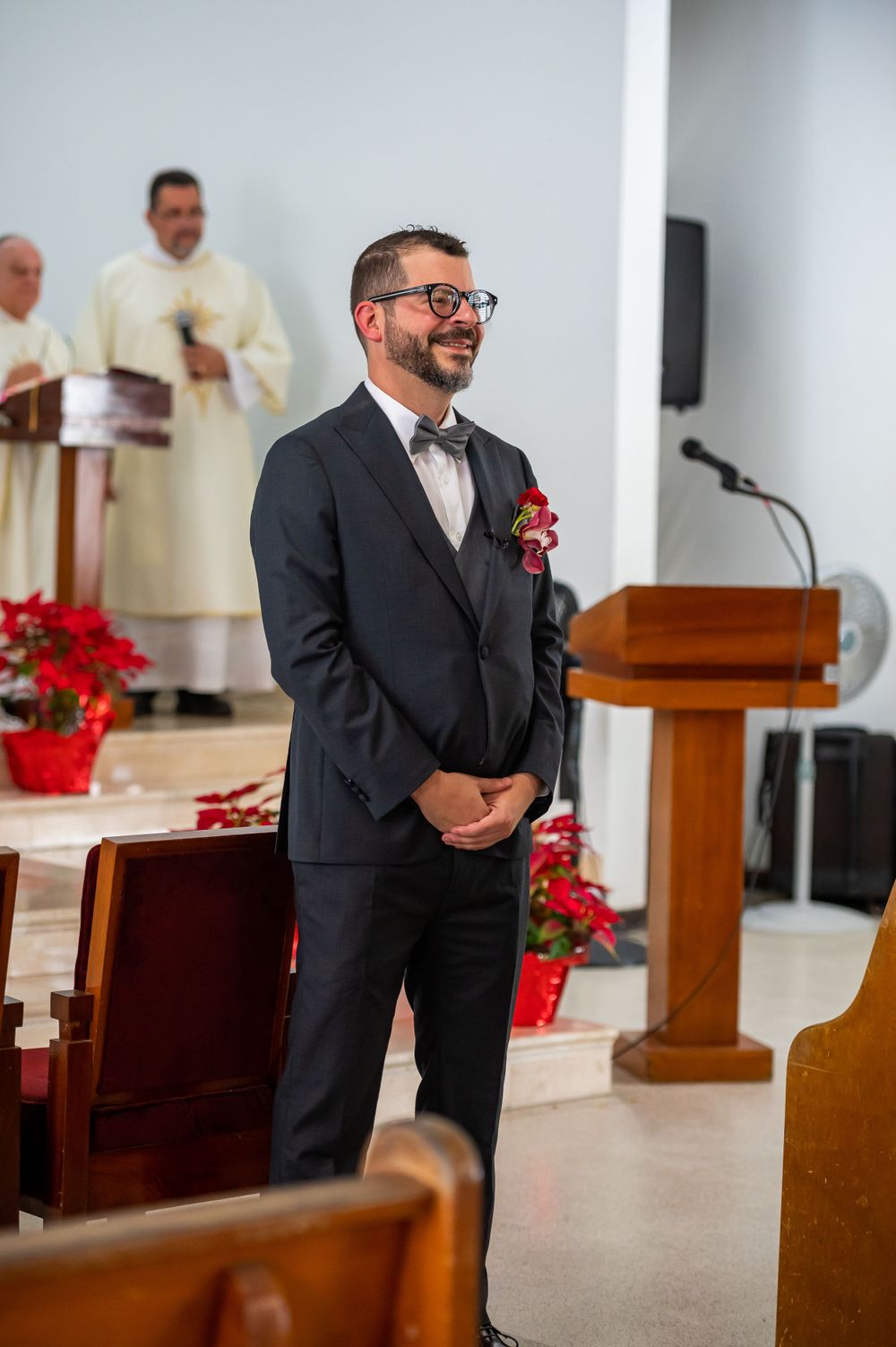 Groom smiles at church altar with priest in white robes visible in background.
