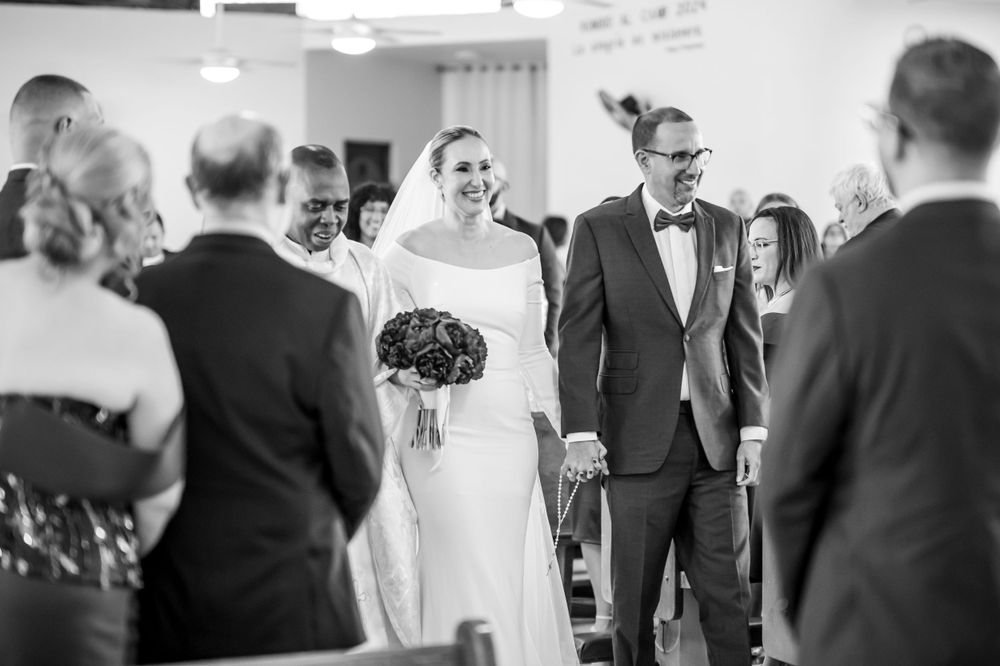 Black and white photo of wedding ceremony with guests looking on as couple walks down aisle.