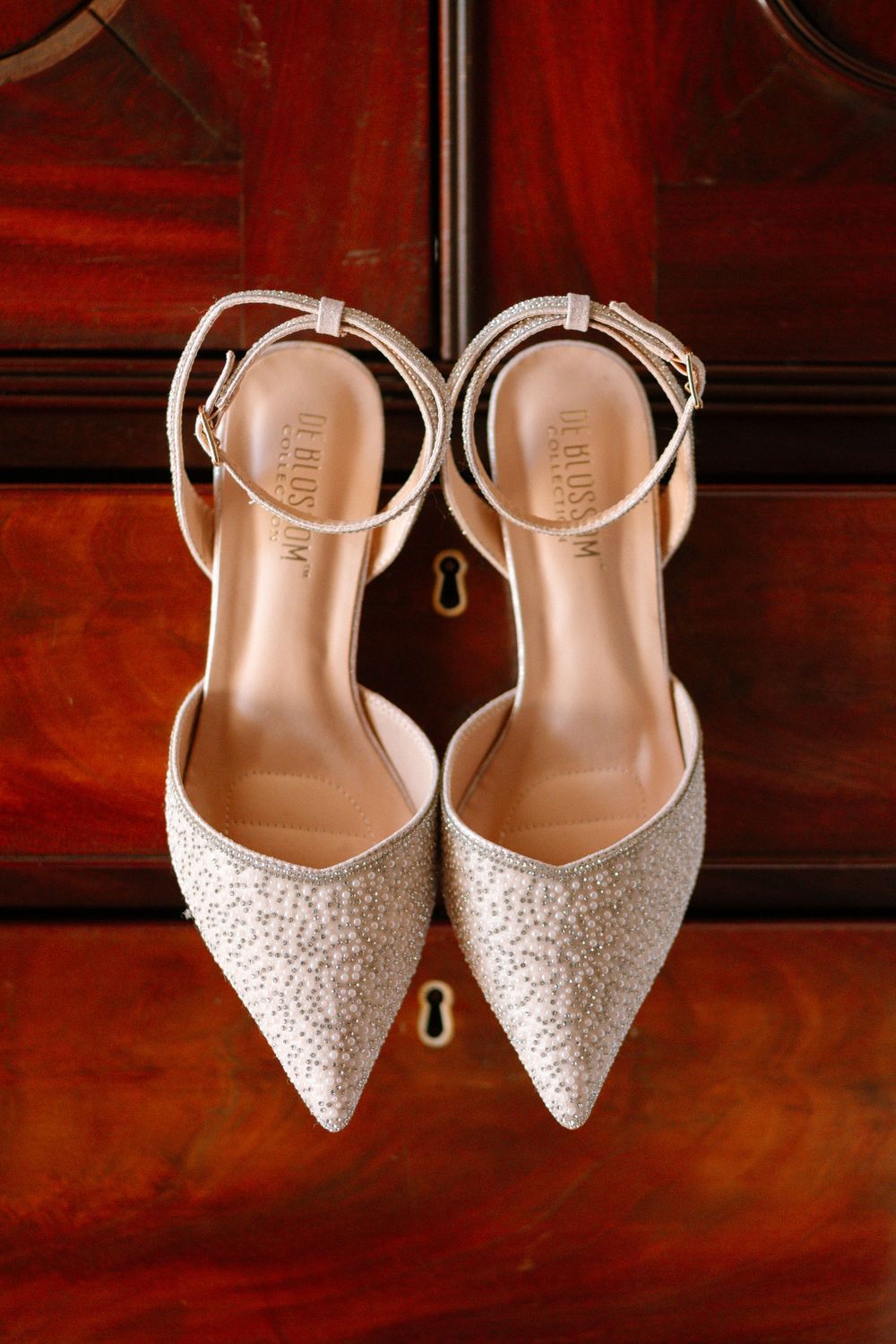 Glittery pointed-toe wedding flats with ankle straps displayed on rich mahogany wood.