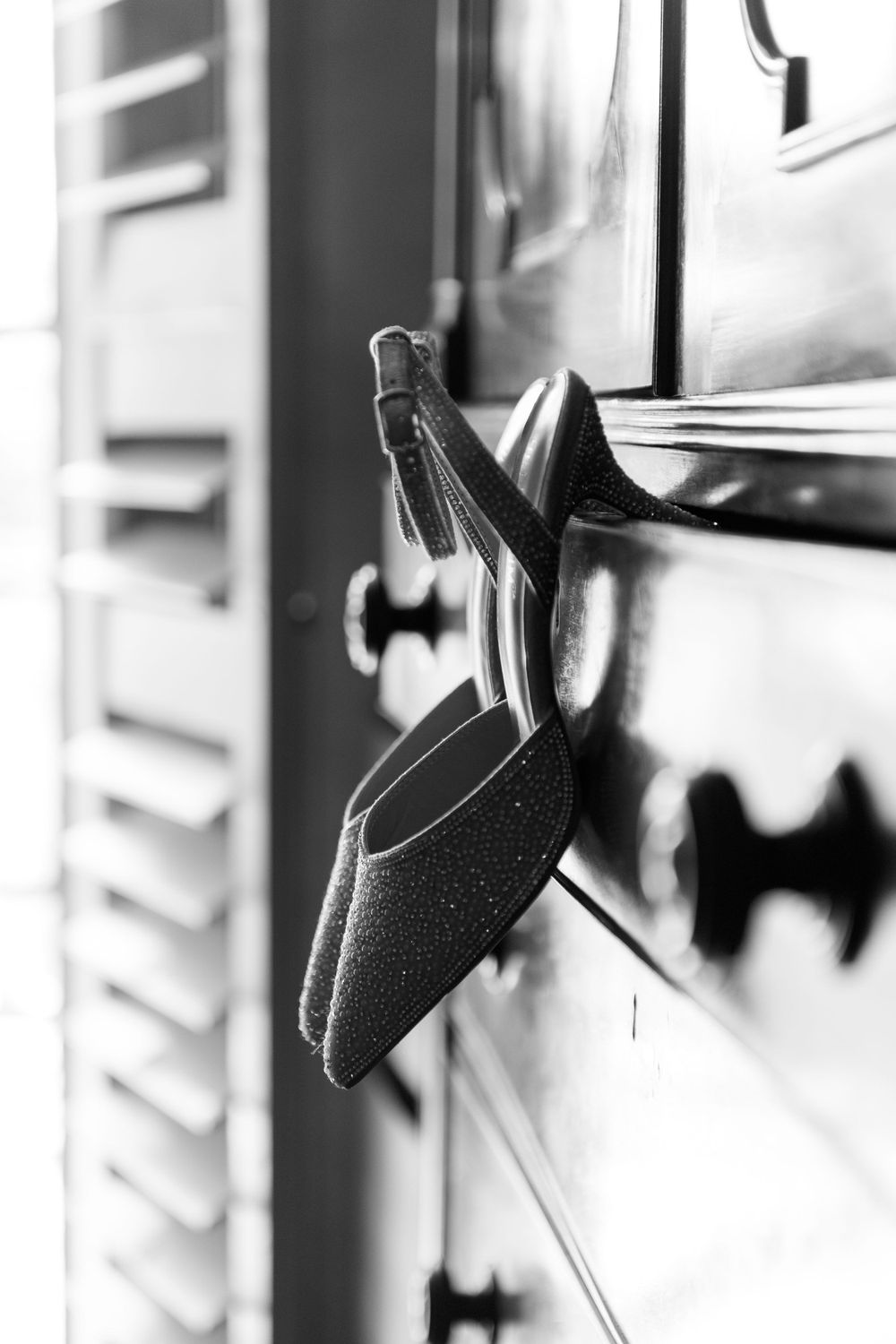 Black and white photo of a sparkly bridal shoe hanging on dresser hardware.