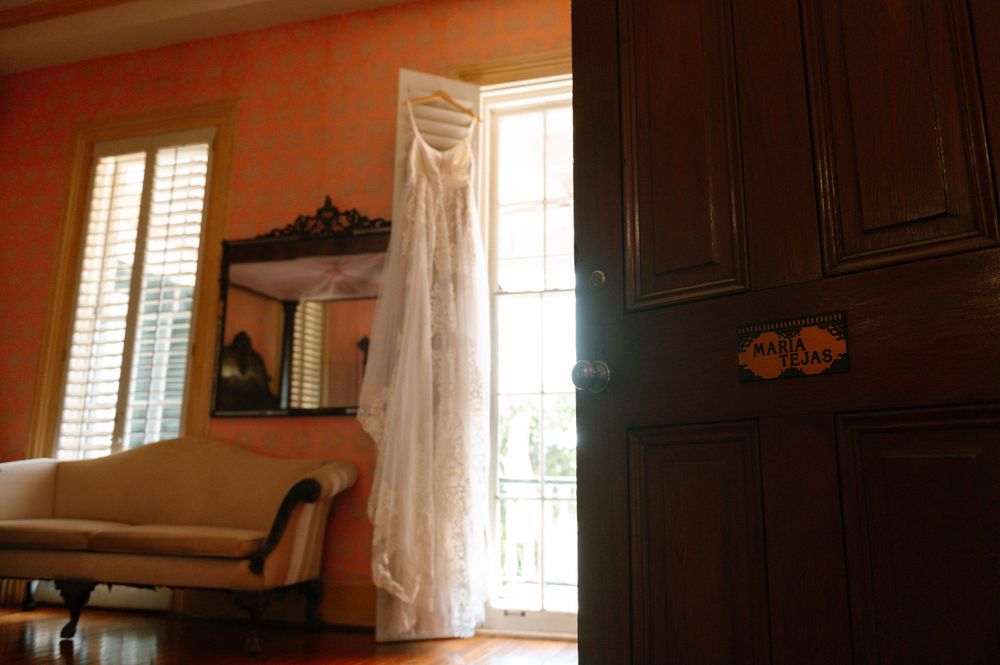 Wedding dress hanging by a window in an elegant room with antique furniture.