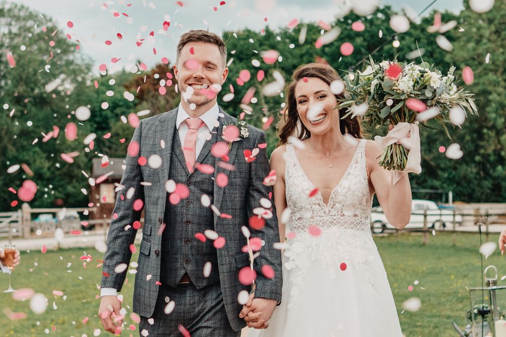 A couple celebrates their wedding day amid a shower of rose petals in a garden setting.