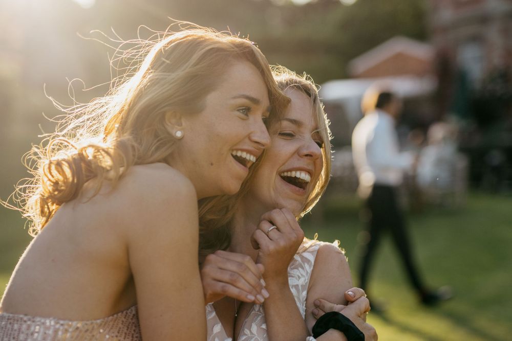 Two friends share a joyful candid moment together during golden hour at an outdoor event.
