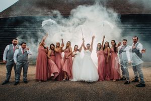 Wedding party celebrates with smoke effects outside rustic building.
