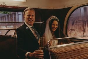 Wedding couple pose in vintage car with champagne glasses.