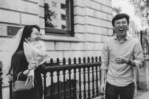 Couple shares a candid moment of laughter by an iron fence in black and white at St Georges Town Hall in London.