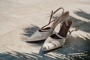 Elegant white wedding heels with slingback straps casting shadows in sunlight in Crete.