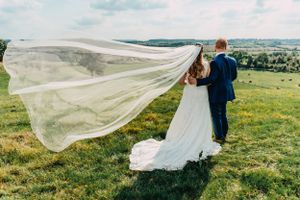 Dramatic shot of flowing wedding veil catching wind on hilltop during sunset.