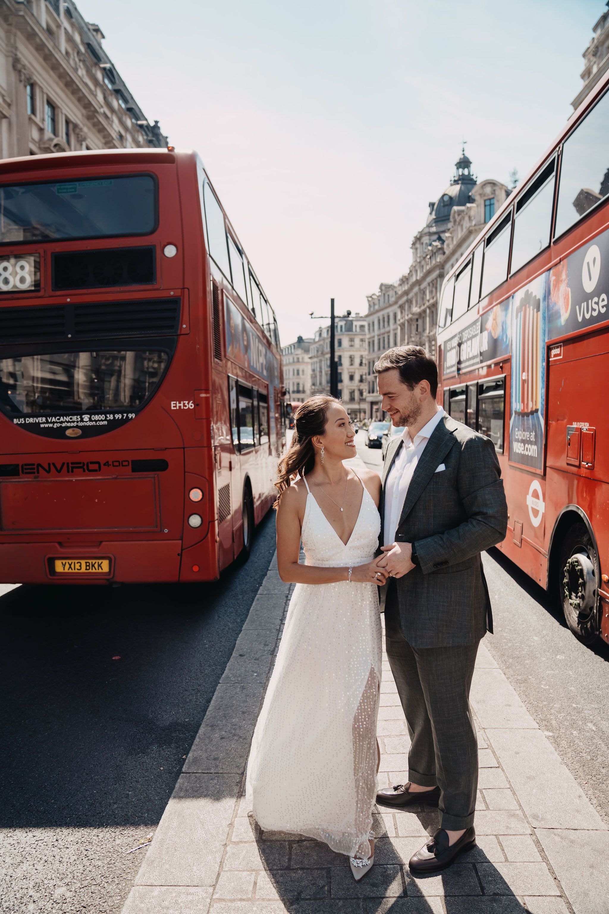 A romantic wedding portrait on a London street with iconic red double-decker buses in the background.