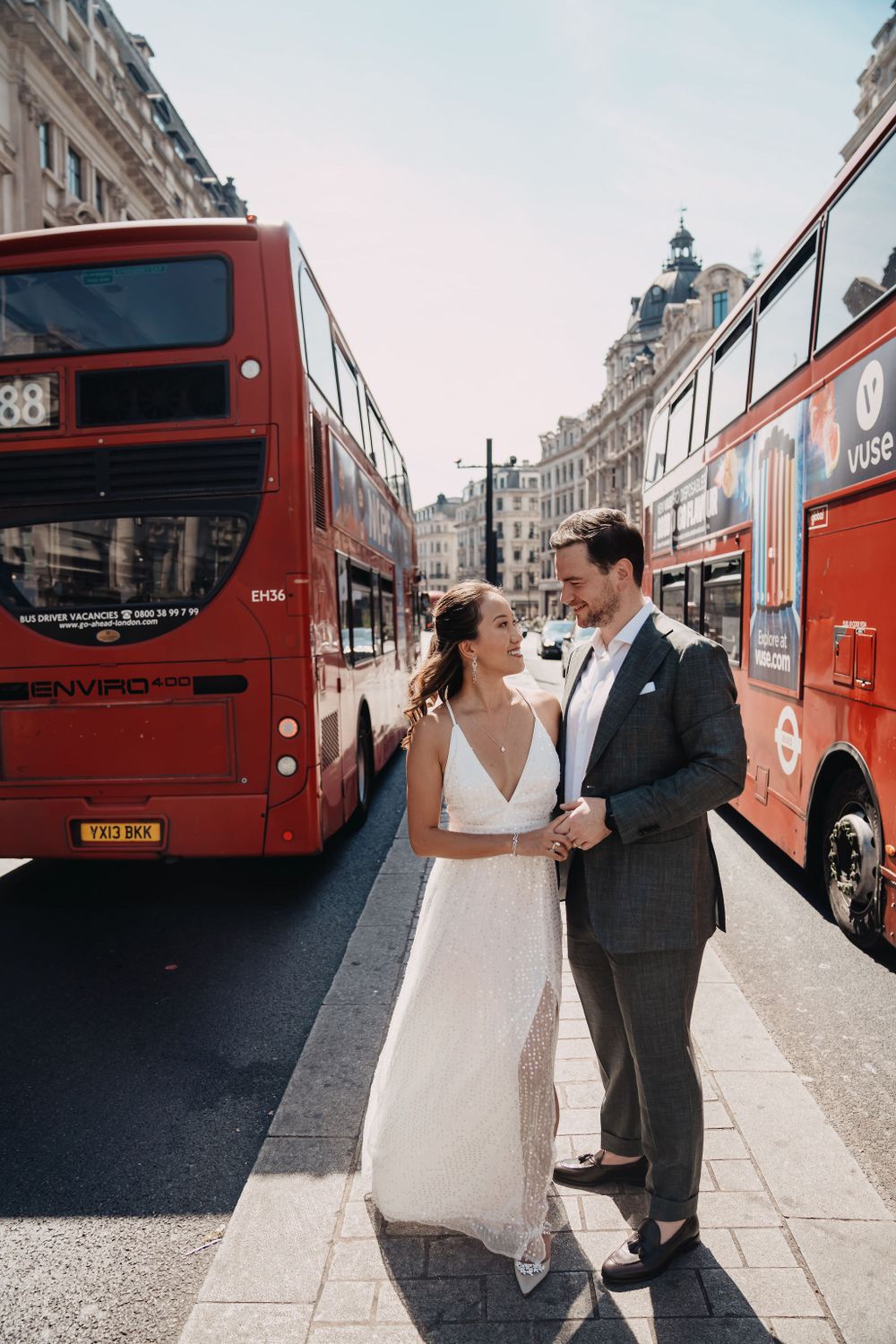 A romantic wedding portrait on a London street with iconic red double-decker buses in the background.