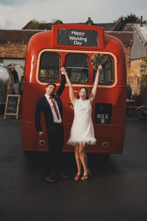 Newlyweds celebrate in front of red vintage bus with Happy Wedding Day sign.