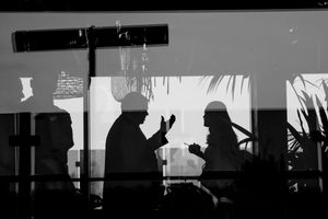 A black and white silhouette of two figures in conversation against a bright window.