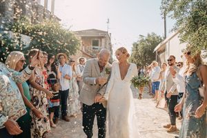 A newlywed couple walks down a flower-lined path while guests shower them with confetti on their wedding day in Crete.