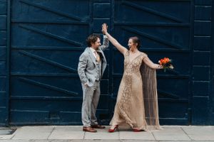 Couple in formal wear dance playfully against blue industrial wall backdrop.