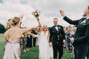 Wedding party celebrates with confetti and raised arms in an outdoor garden ceremony at Ham Polo Club.