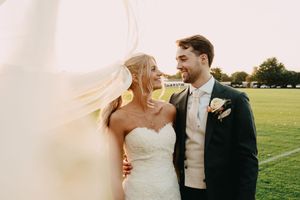 A couple shares an intimate wedding day moment on an open field as the bride's veil catches the wind at Ham Polo Club.
