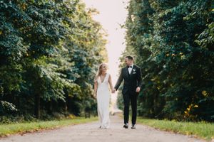 Newlyweds walk hand in hand down a tree-lined path on their special day at Ham Polo Club.