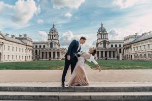 A wedding couple poses playfully on the steps of  the Greenwich Royal Naval College with symmetrical domed architecture.