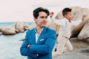 Men in contrasting suits pose artistically by coastal rocks, in Sardinia.