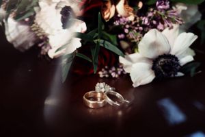 Wedding rings displayed with white anemone flowers and delicate florals in dark moody setting.