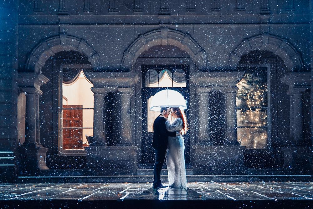 A romantic silhouette at a stone archway in the rain creates a dreamy wedding portrait.