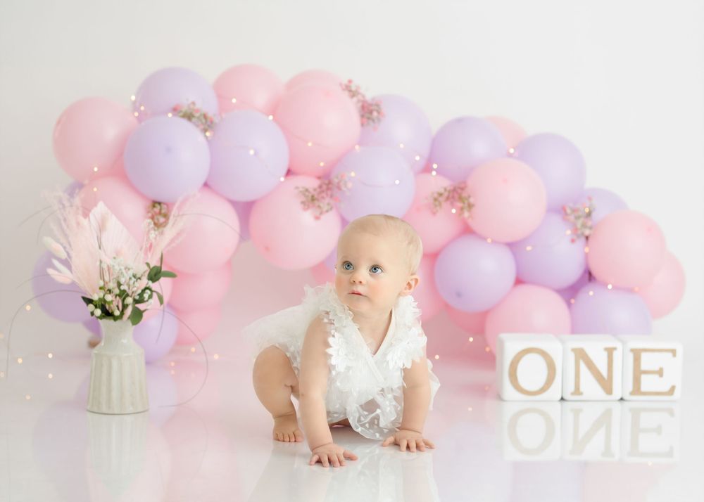 Crawling pose against pastel balloon wall with ONE blocks and white floral decor.
