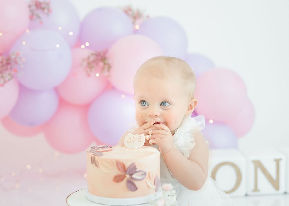 Cake tasting moment with pink frosted cake against pastel balloon background.