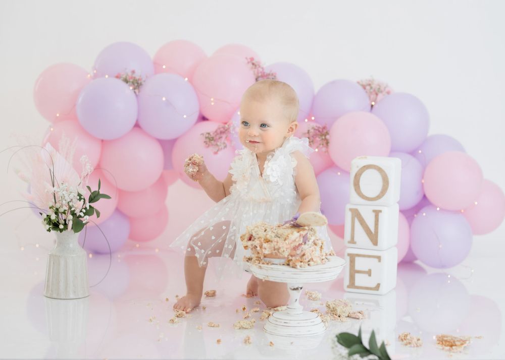 Joyful cake smash moment with scattered crumbs against pastel balloon wall.