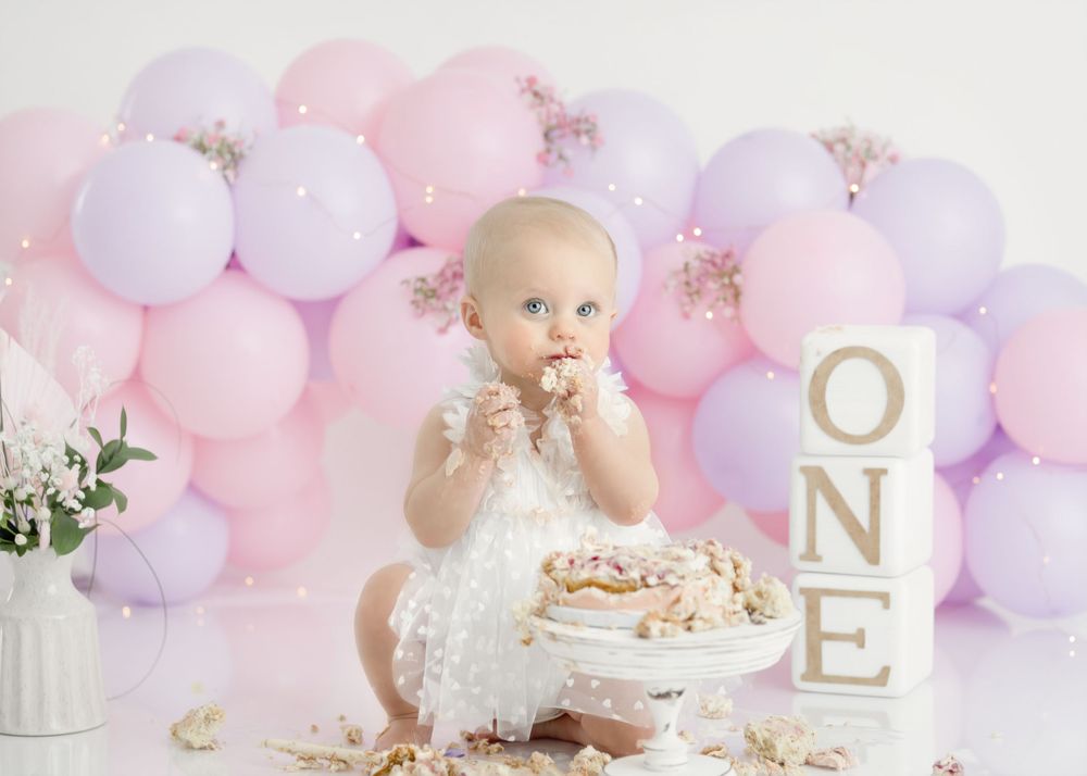 Messy cake smash photography setup with white dress and decorative balloon arch.