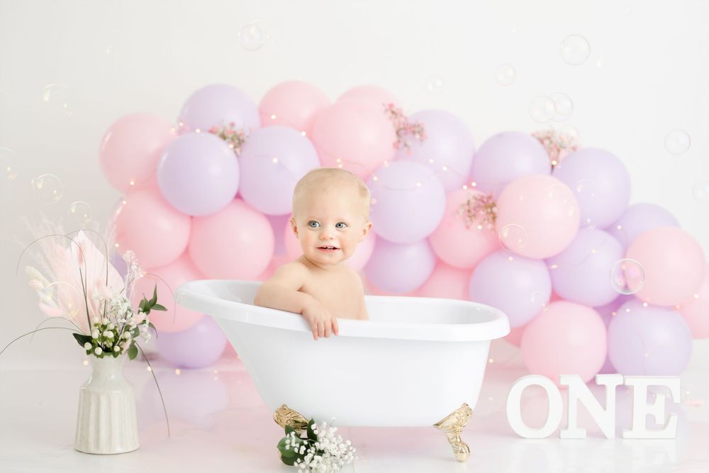 White bathtub photo setup with pink and purple balloon backdrop and ONE lettering.