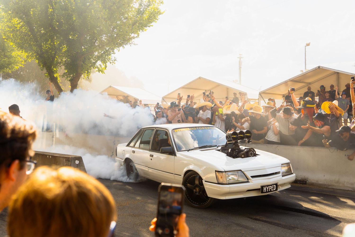 Car performing burnout demonstration with smoke for crowd at automotive event.