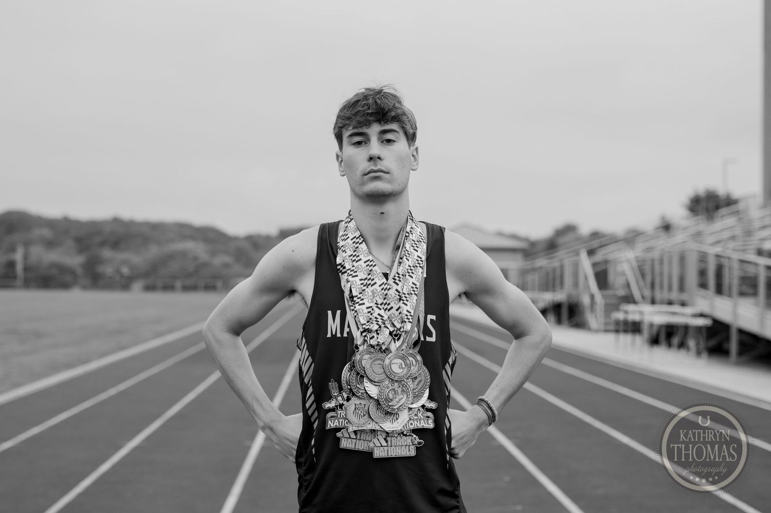 A black and white portrait of an athlete wearing medals on a track field.