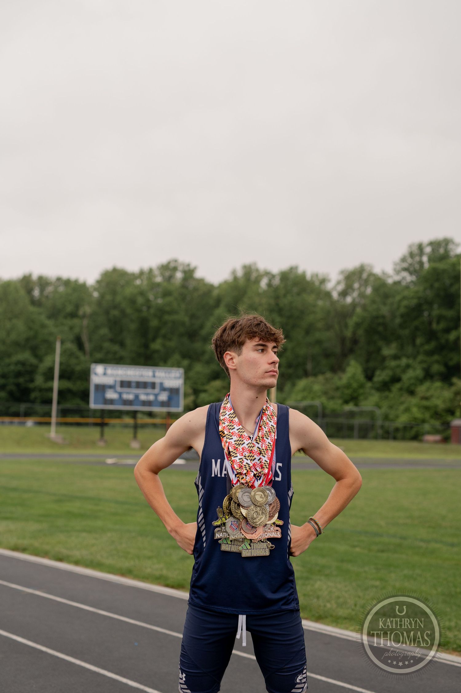 An athlete stands on a running track wearing a navy uniform with multiple medals around their neck.