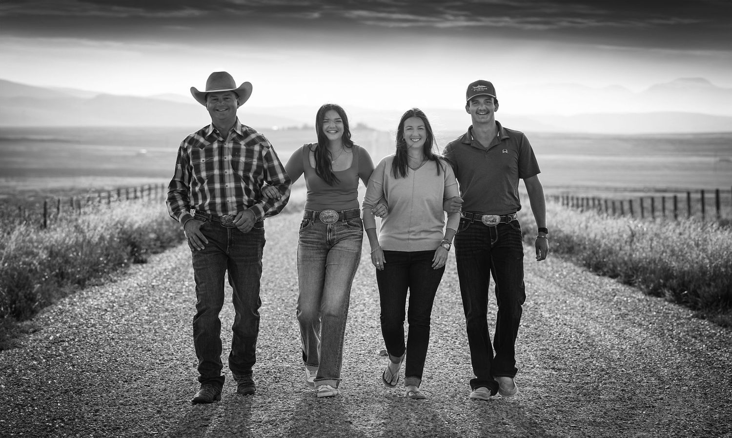 Family of four walking together on rural road in black and white photo.