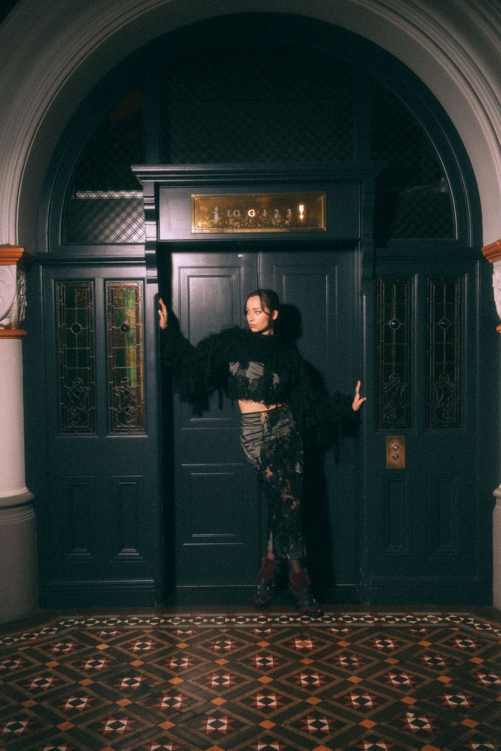 Gothic architectural setting with ornate doorway and patterned floor in moody lighting.