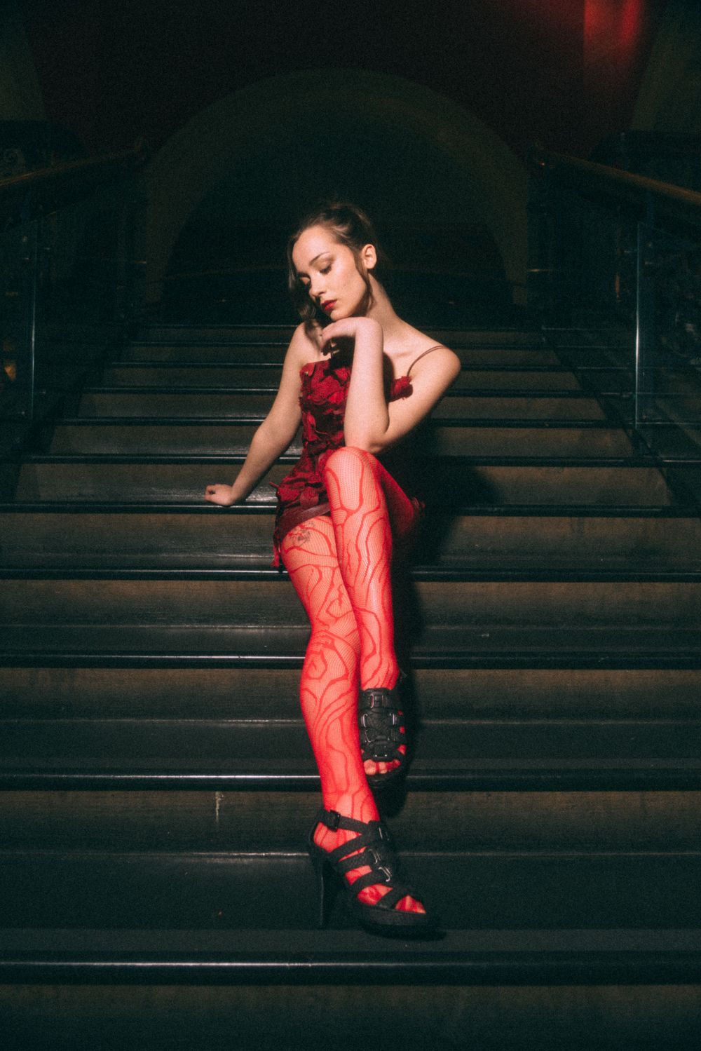 Dramatic pose on dark staircase wearing red dress and patterned stockings.