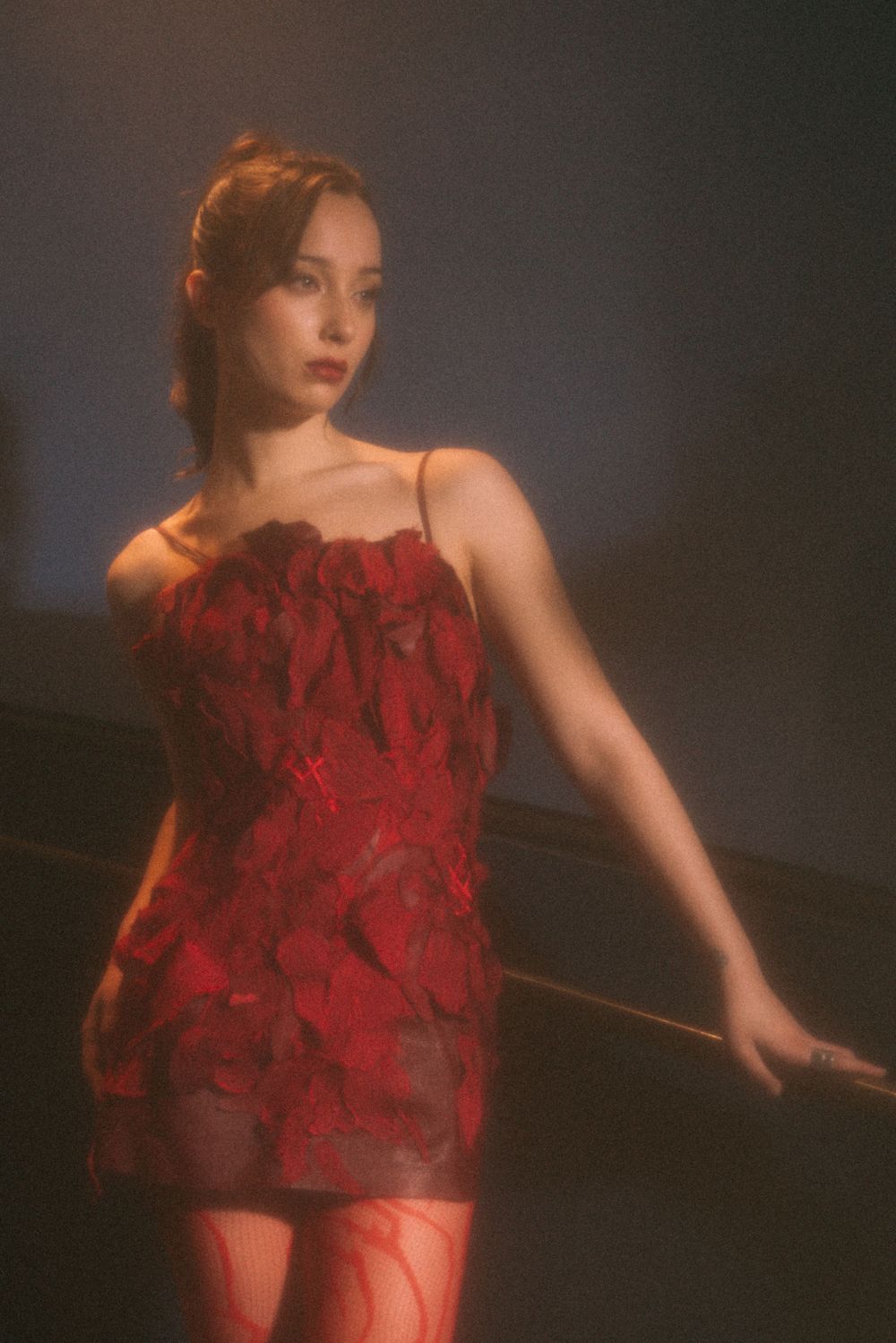 Atmospheric portrait shot featuring a sheer red dress against a dark background.