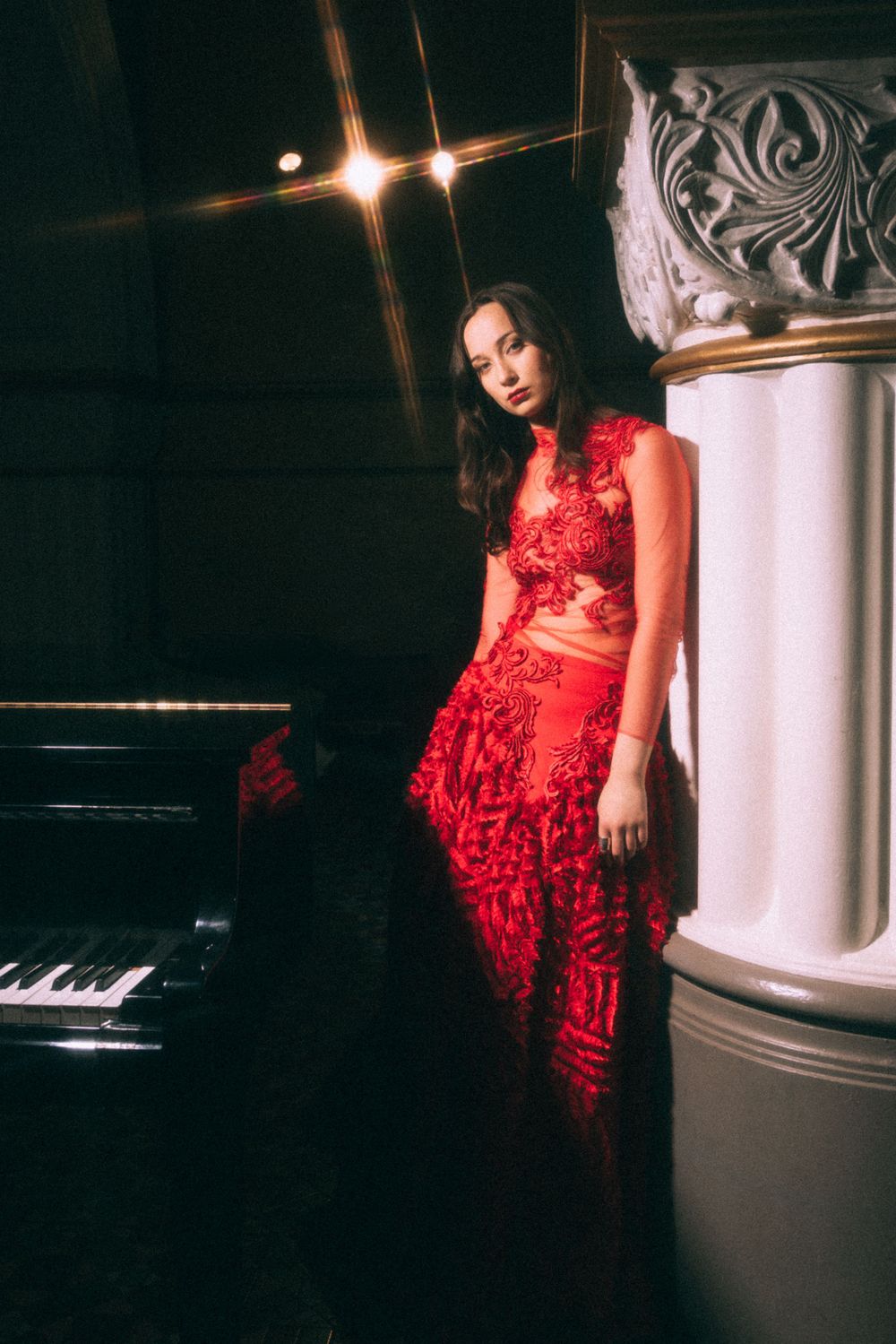 Elegant scene with a piano and ornate column featuring red formal attire.