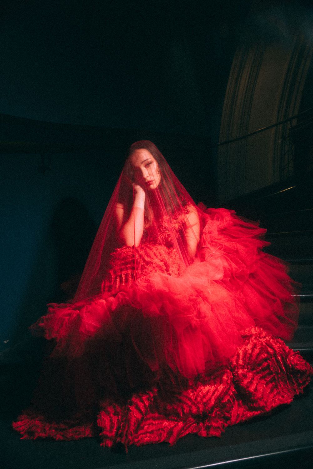 Dramatic fashion photograph featuring a voluminous red gown in dark setting.