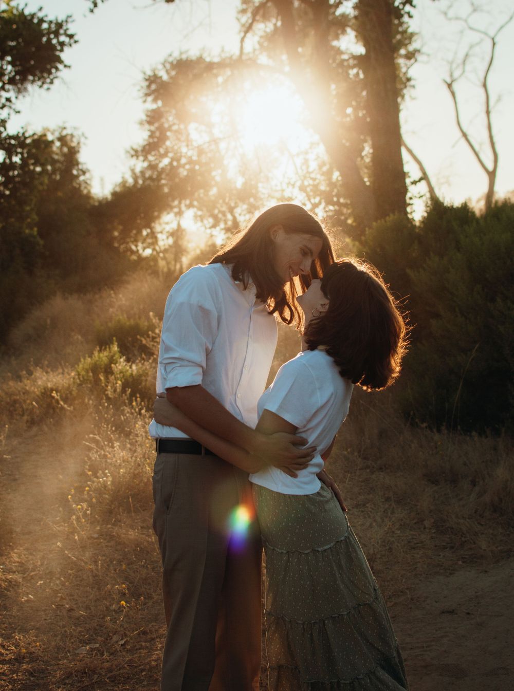 A romantic sunset portrait of a couple embracing with golden sunlight filtering through trees.