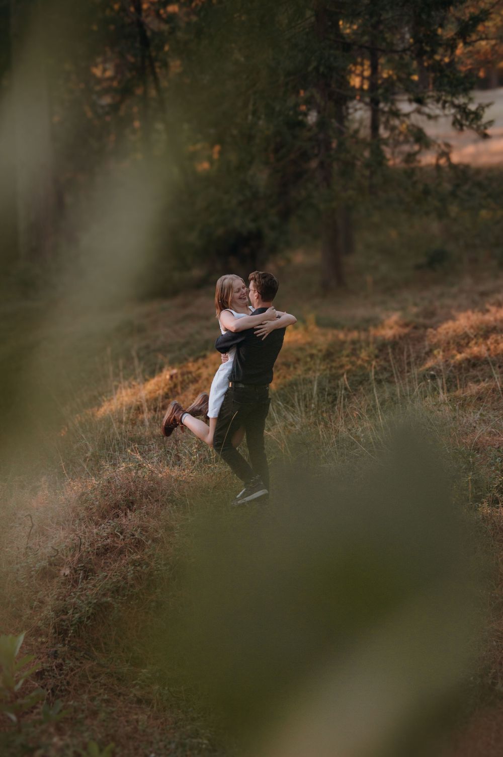 A couple embraces in a romantic dance pose against a dreamy golden sunset backdrop in a grassy meadow.