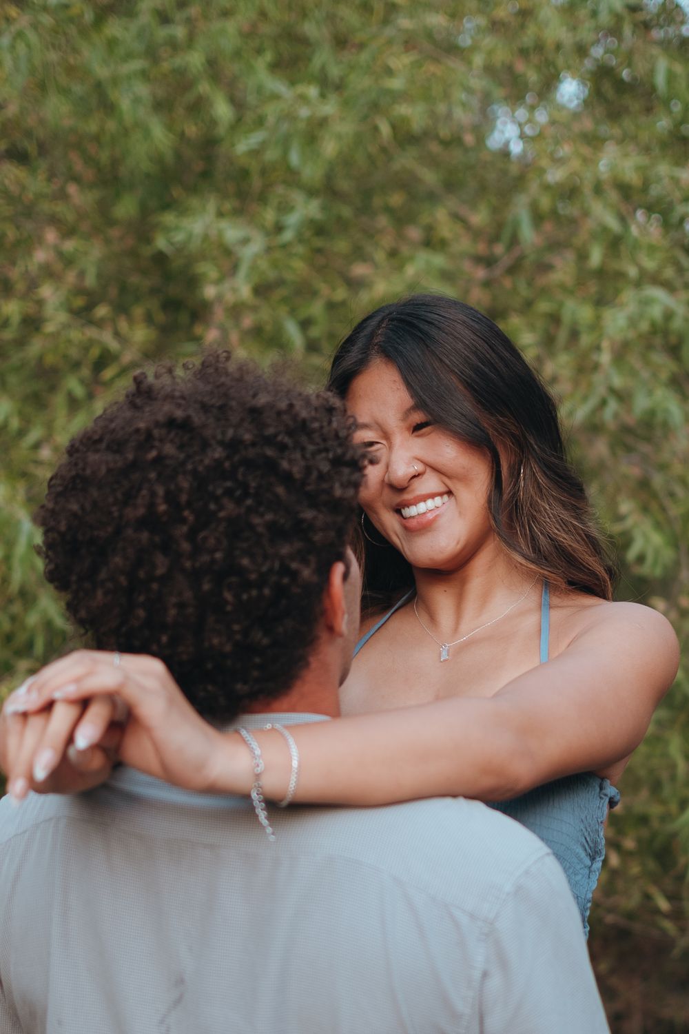 A couple shares a tender romantic moment outdoors with soft natural lighting and greenery in the background.